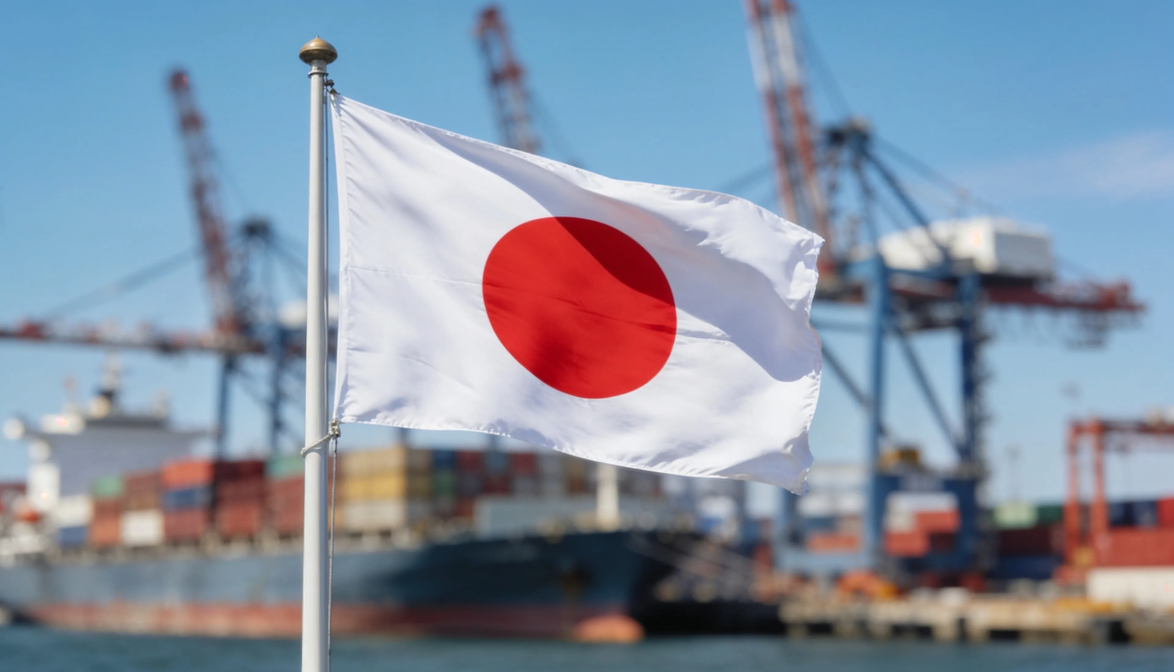 Flag of Japan flying over a container harbour - marine spare parts delivered to Japan from India